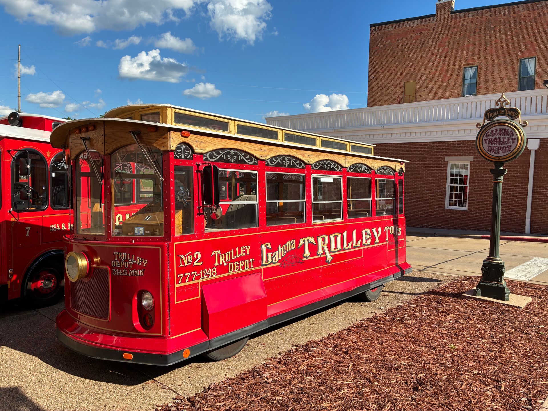 A red and white trolley on a city street, with brick buildings, power lines, and a crosswalk.
