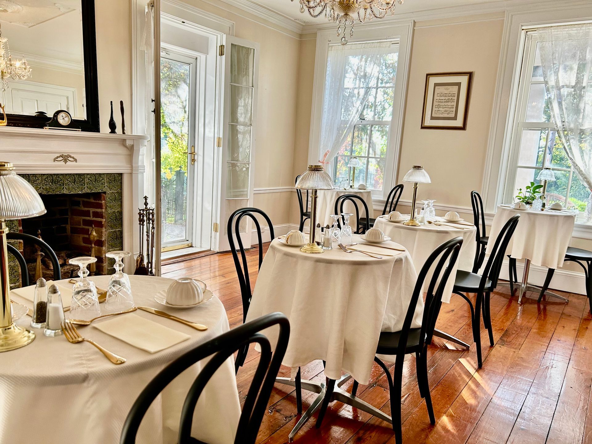 Dining room with round tables, white tablecloths, black chairs, and a chandelier.