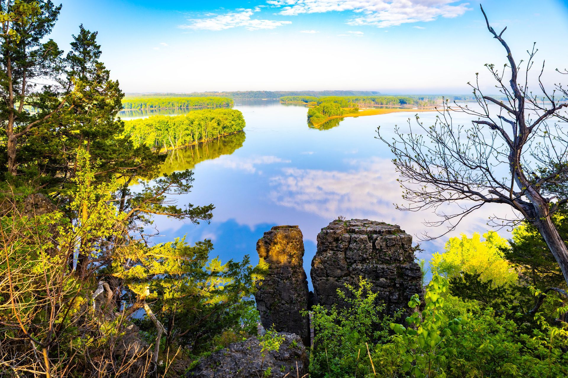 Scenic lake view framed by green trees and rocky cliffs under a bright blue sky
