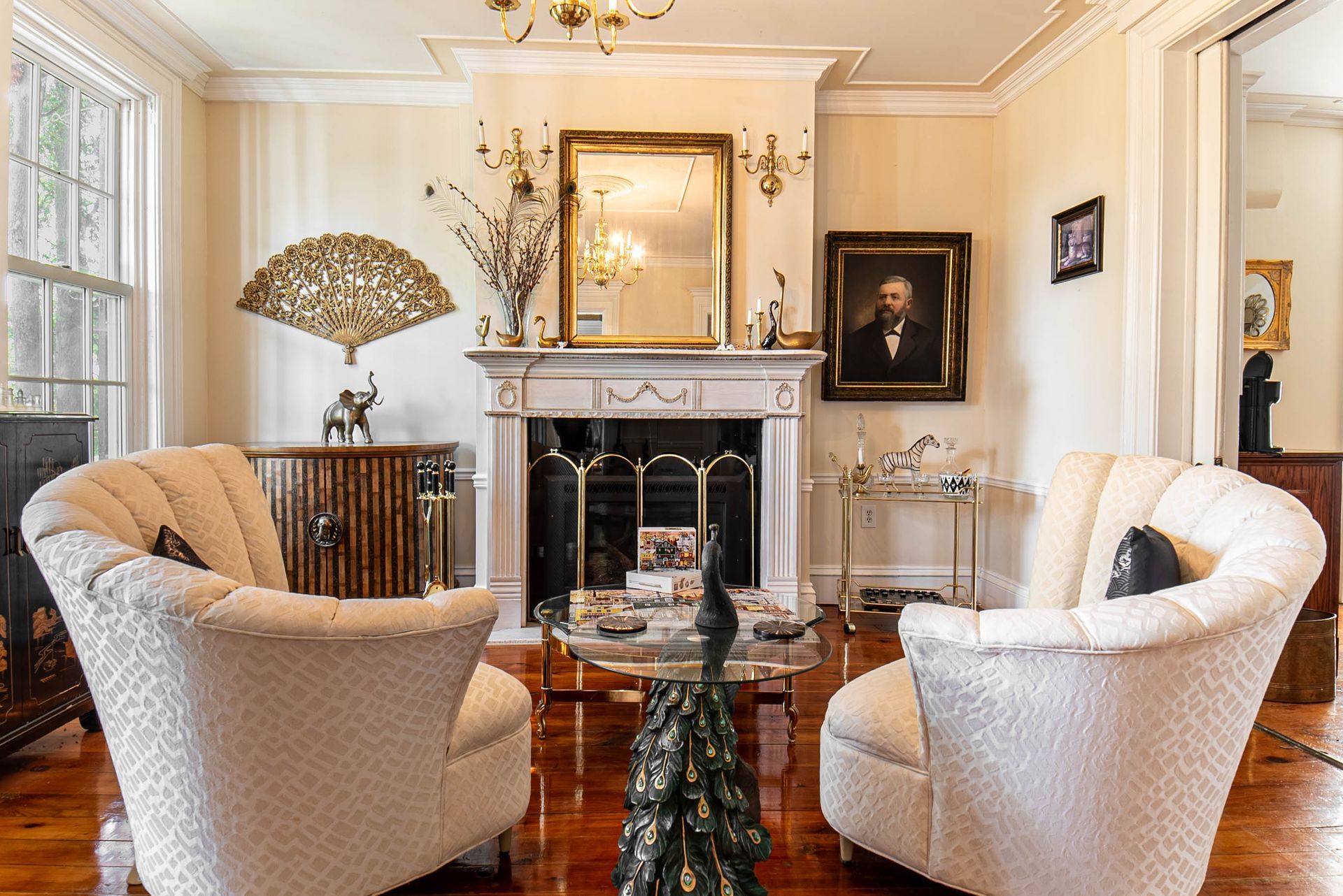 Cozy living room with fireplace, two armchairs, ornate decor, and hardwood floor.