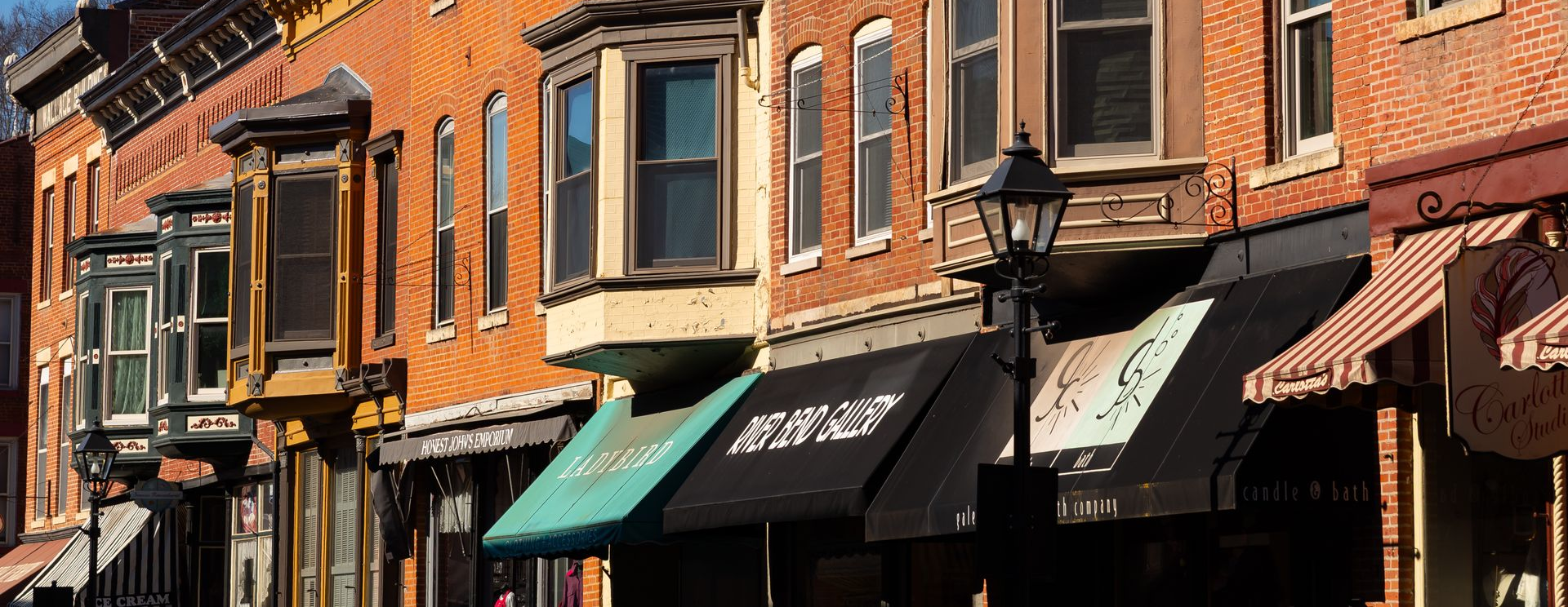 Brick storefronts with striped awnings and hanging signs on a sunny street corner