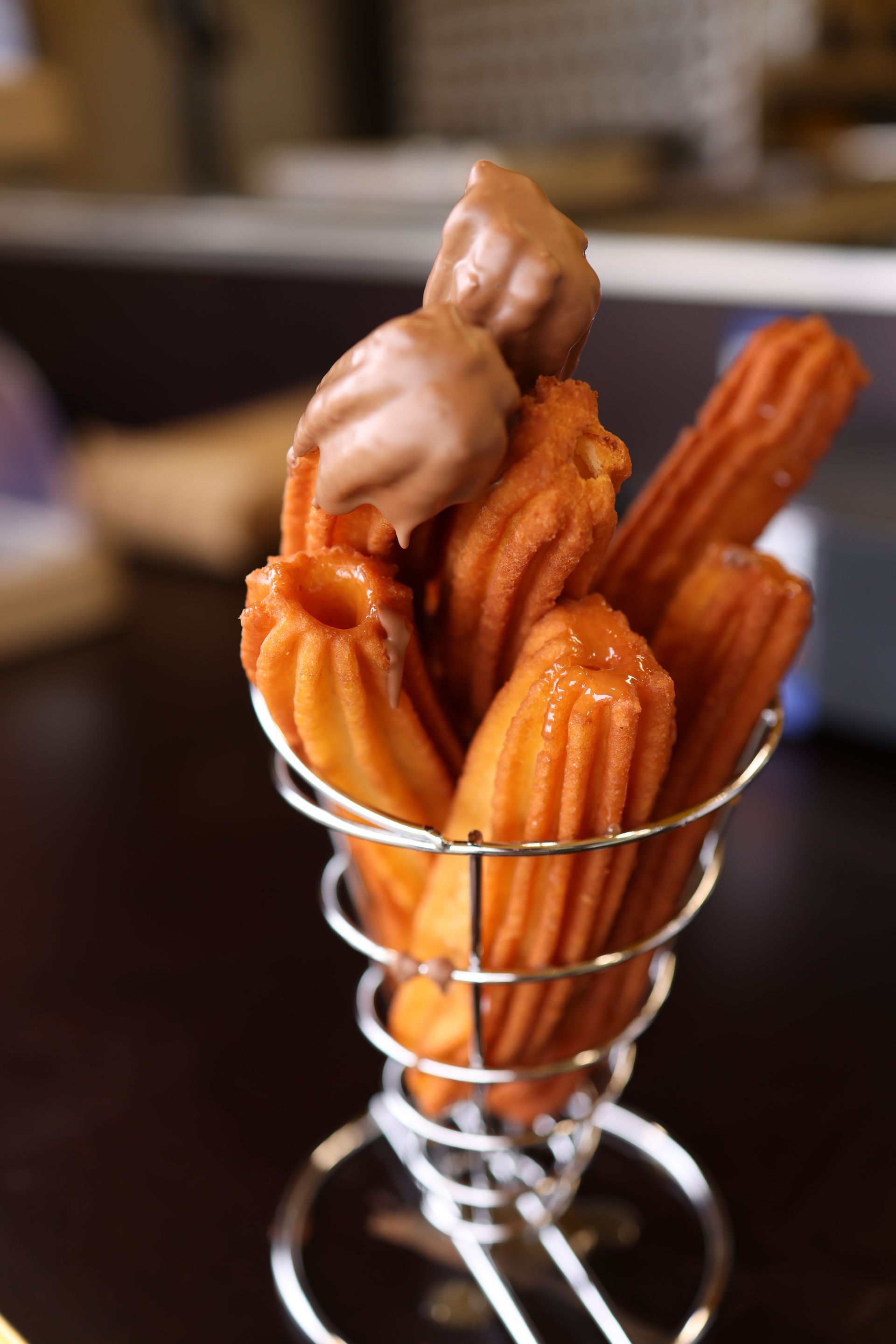 Hand holding a tray of churros with various toppings, in front of a turquoise food truck sign,