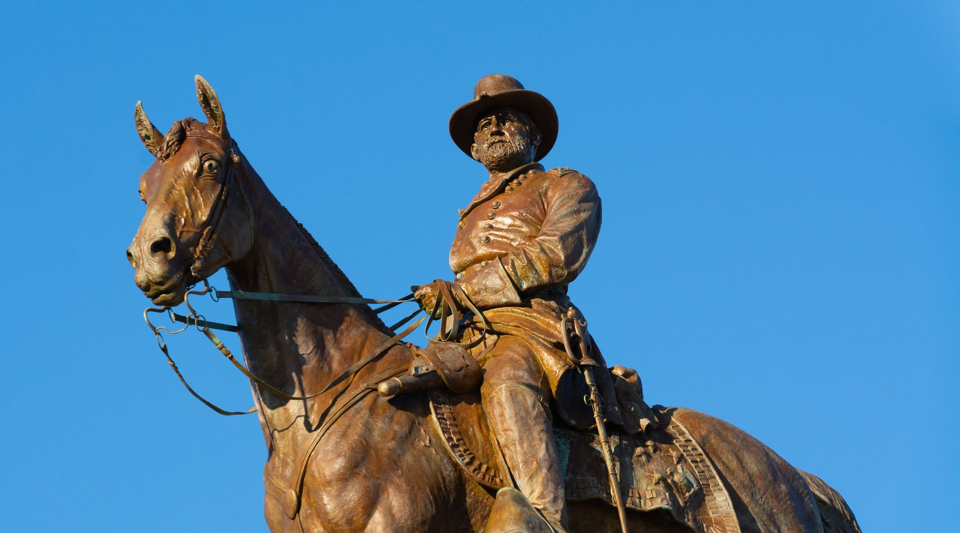 Bronze cowboy statue on horseback against a clear blue sky