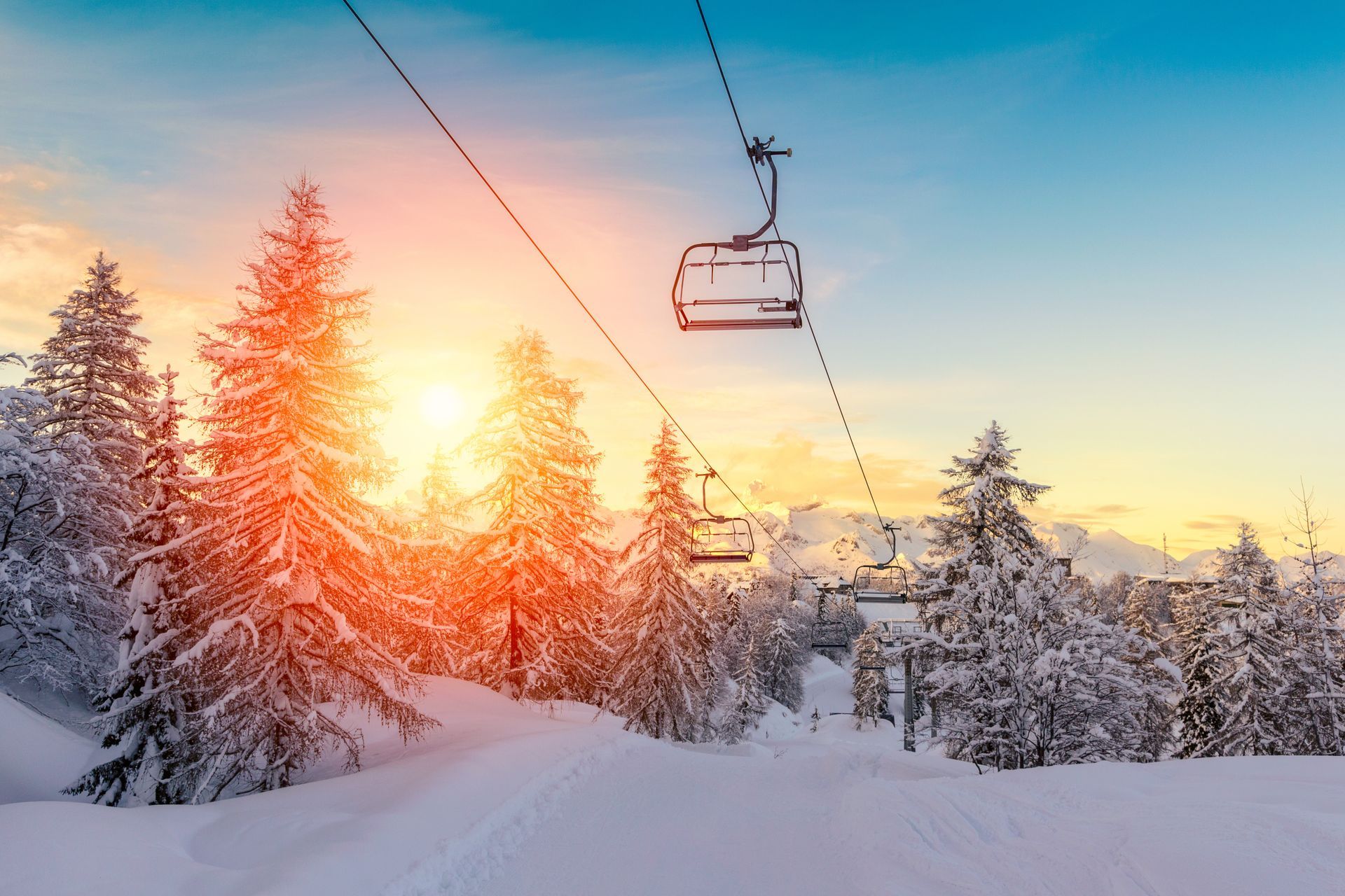 Snowy forest with ski lift at sunset, golden sun glowing over frosted trees and a winter trail