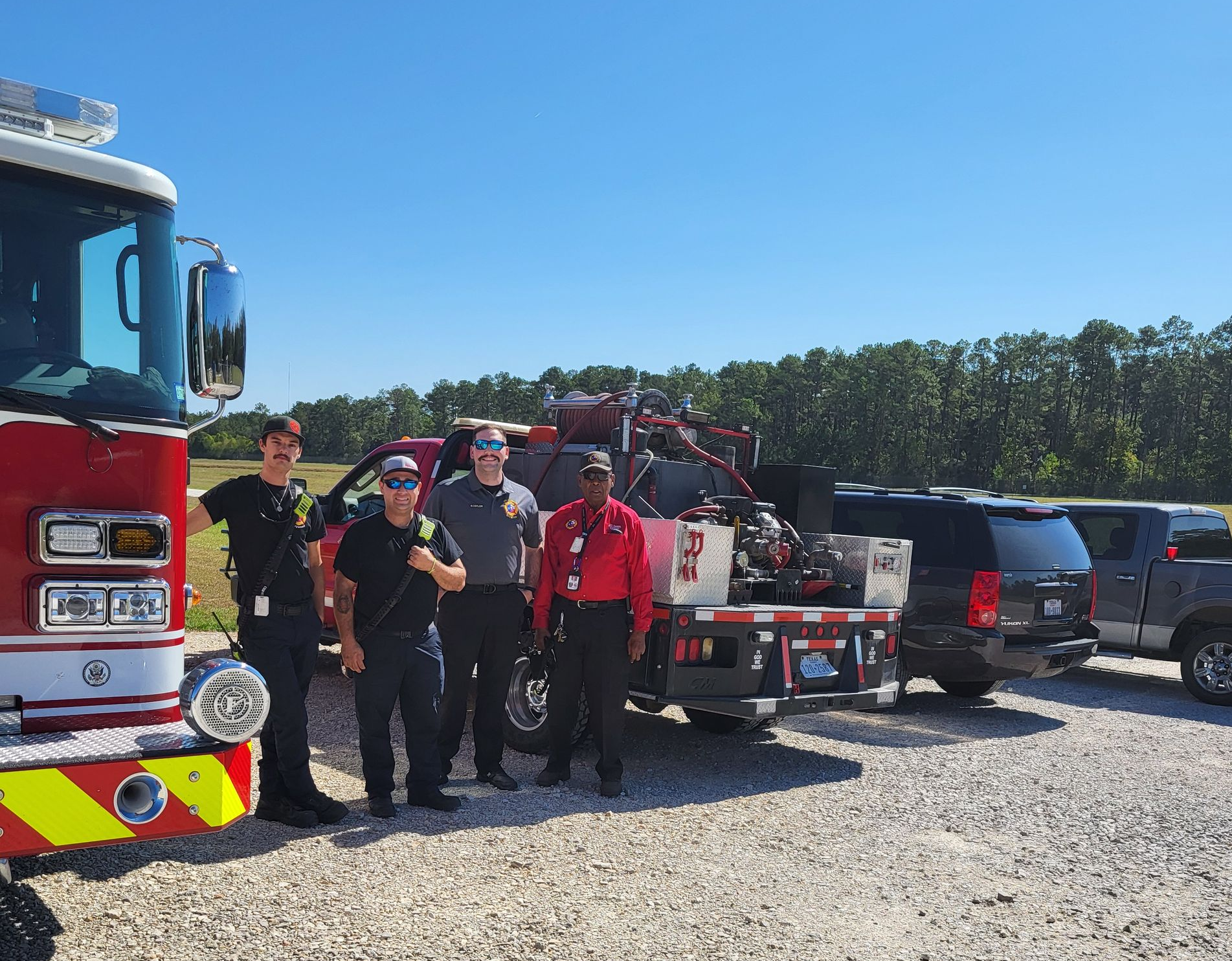 Firefighters standing near a fire truck holding equipment on a sunny day.