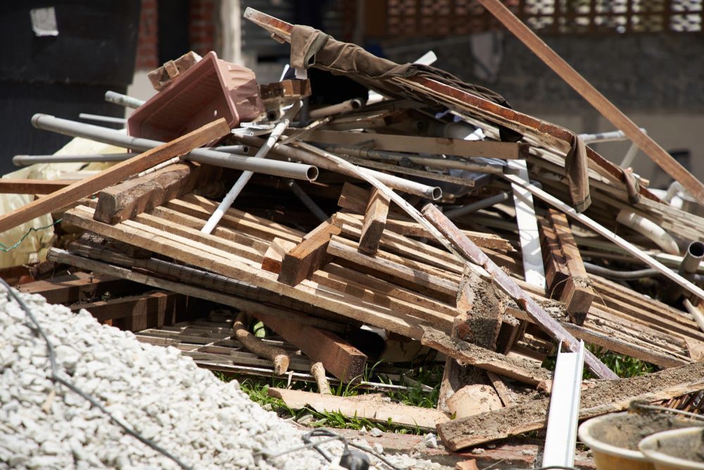 A pile of construction debris featuring wooden pallets, metal pipes, and gravel on a building site.