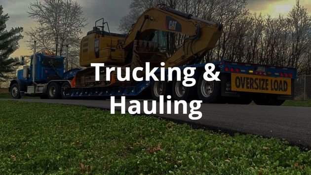 A truck from R. Work Excavating & Trucking is hauling a bulldozer down a road.