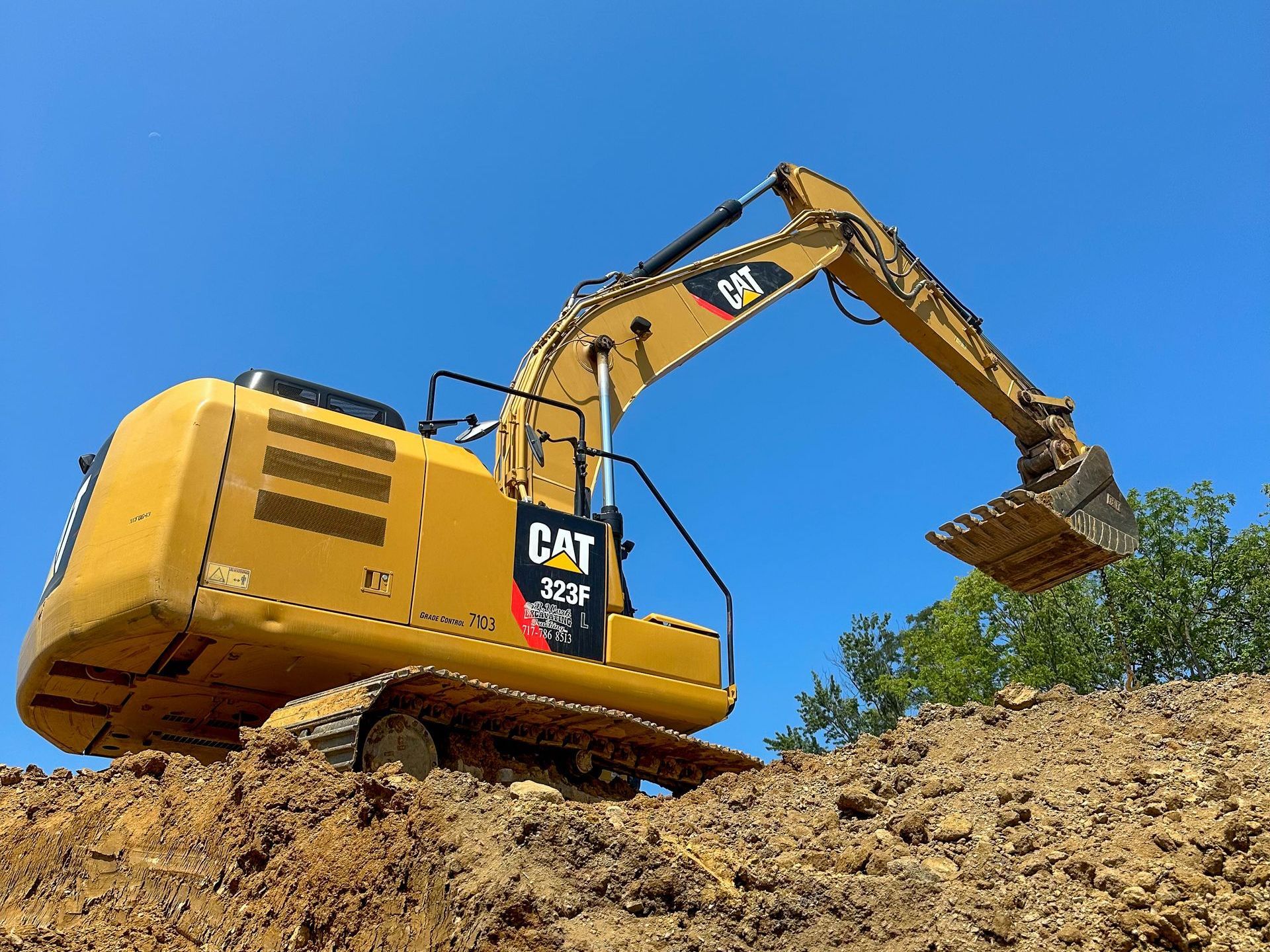 A yellow cat excavator from R. Work Excavating & Trucking is sitting on top of a pile of dirt.
