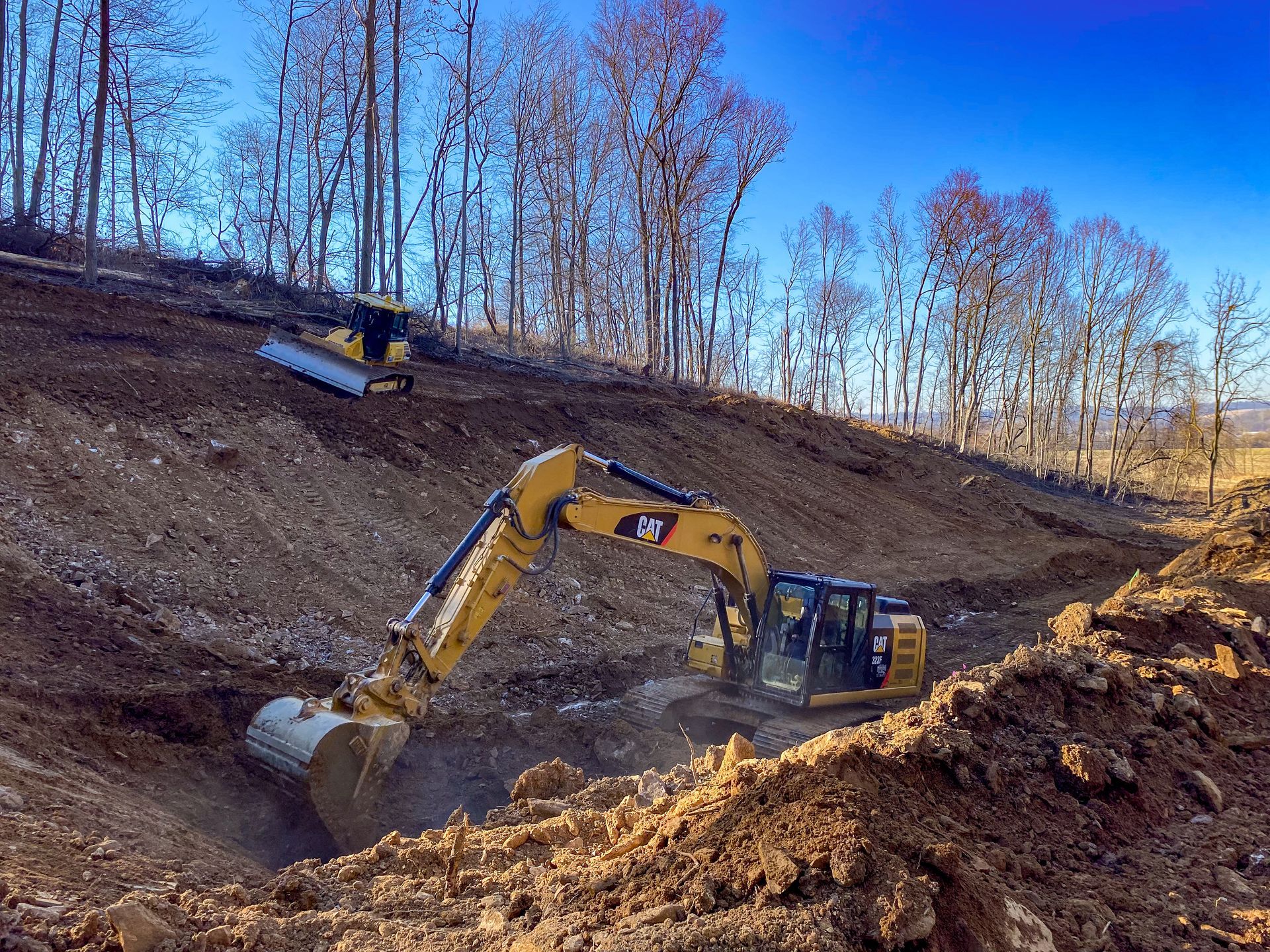 A yellow excavator from R. Work Excavating & Trucking is digging a hole in the dirt on a hill.