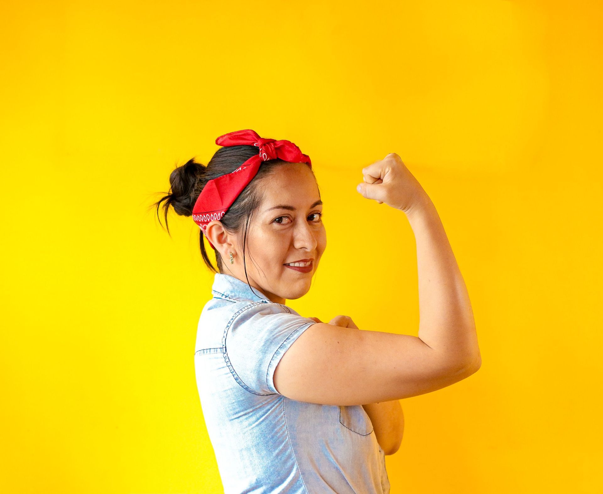 Strong working women flexing with her shirt sleeve rolled up and a bandana in her hair.