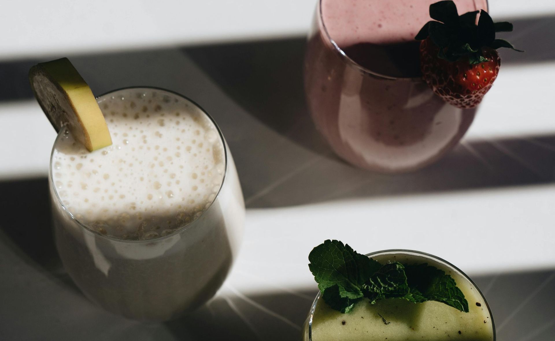 Three smoothies are sitting on a table with strawberries and mint leaves.