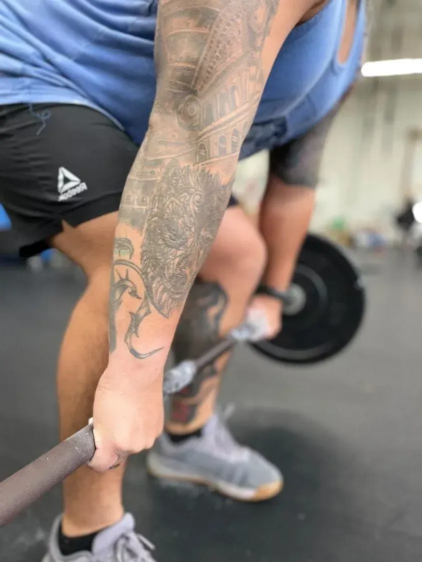 A man with a tattoo on his arm is lifting a barbell in a gym.