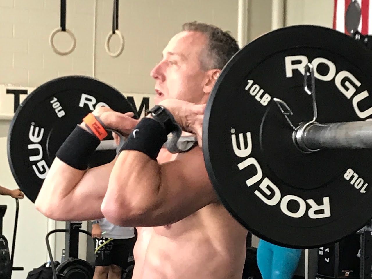 A man is squatting with a barbell that says rogue on it