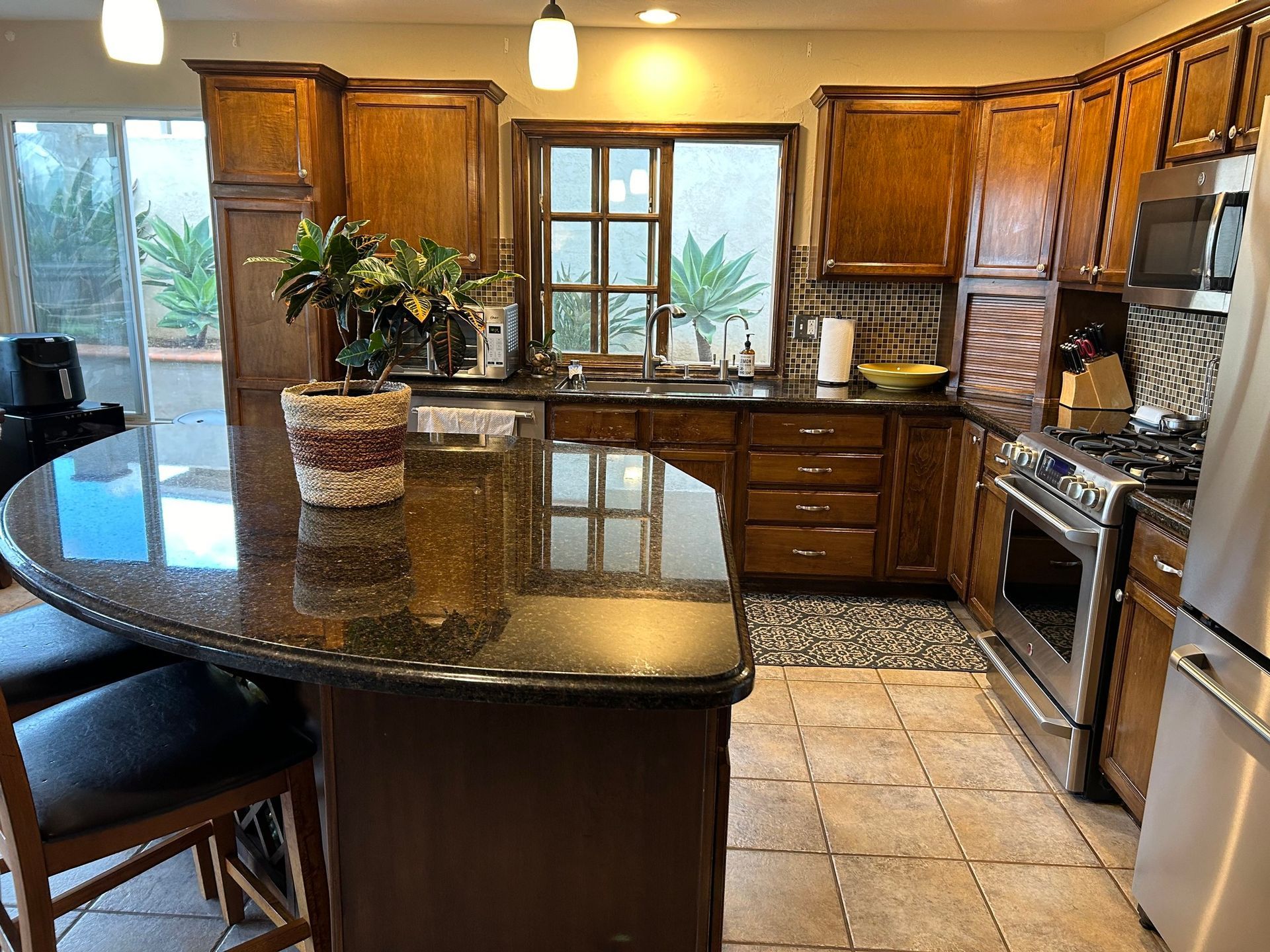 Kitchen with wood cabinets, granite countertop island with stools, stainless steel appliances, and a window.