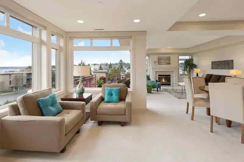 Bright living room with beige sofas, teal pillows, and large windows overlooking a scenic view
