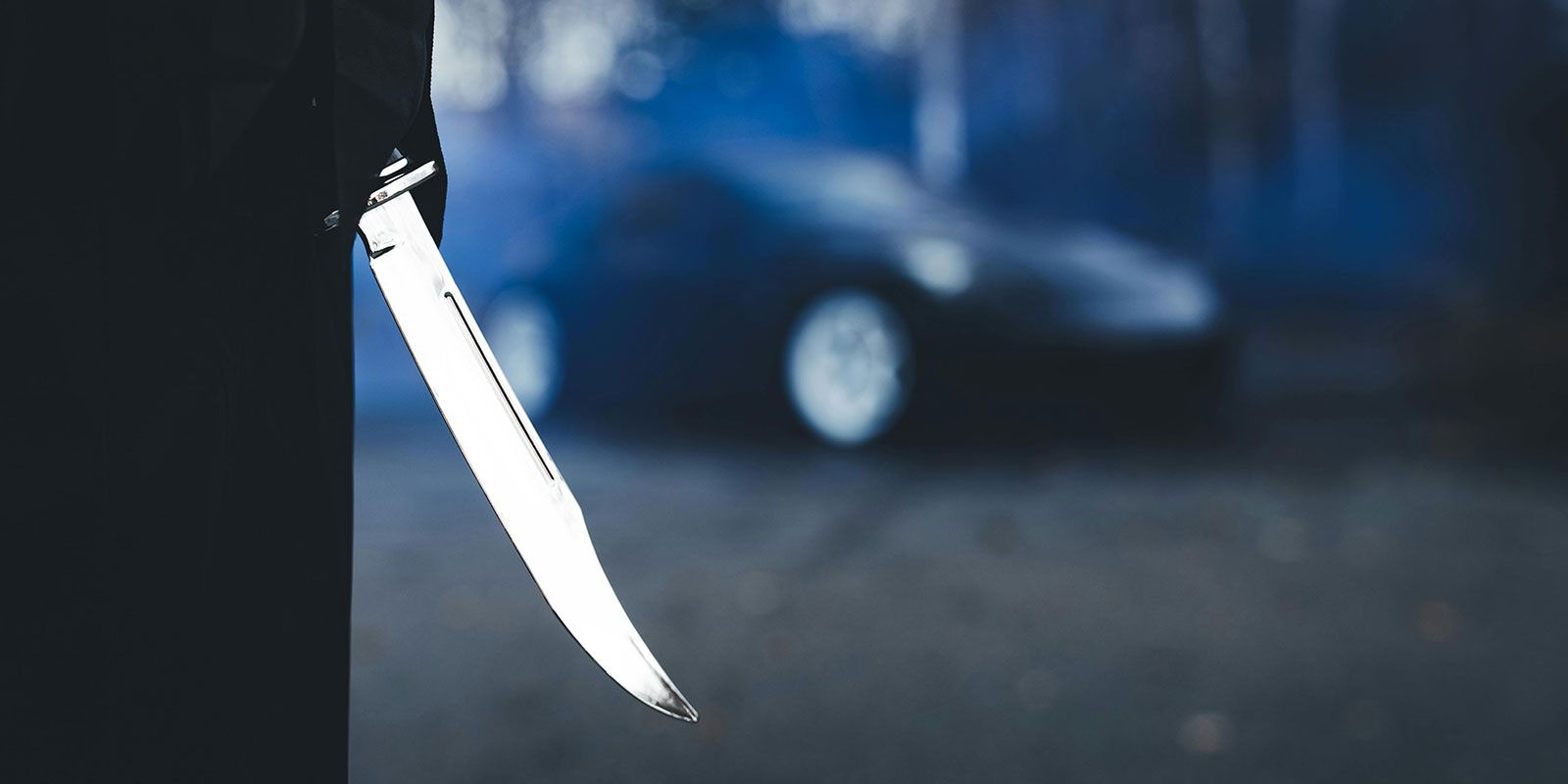 A knife blade in sharp focus with a blurred car in the background.