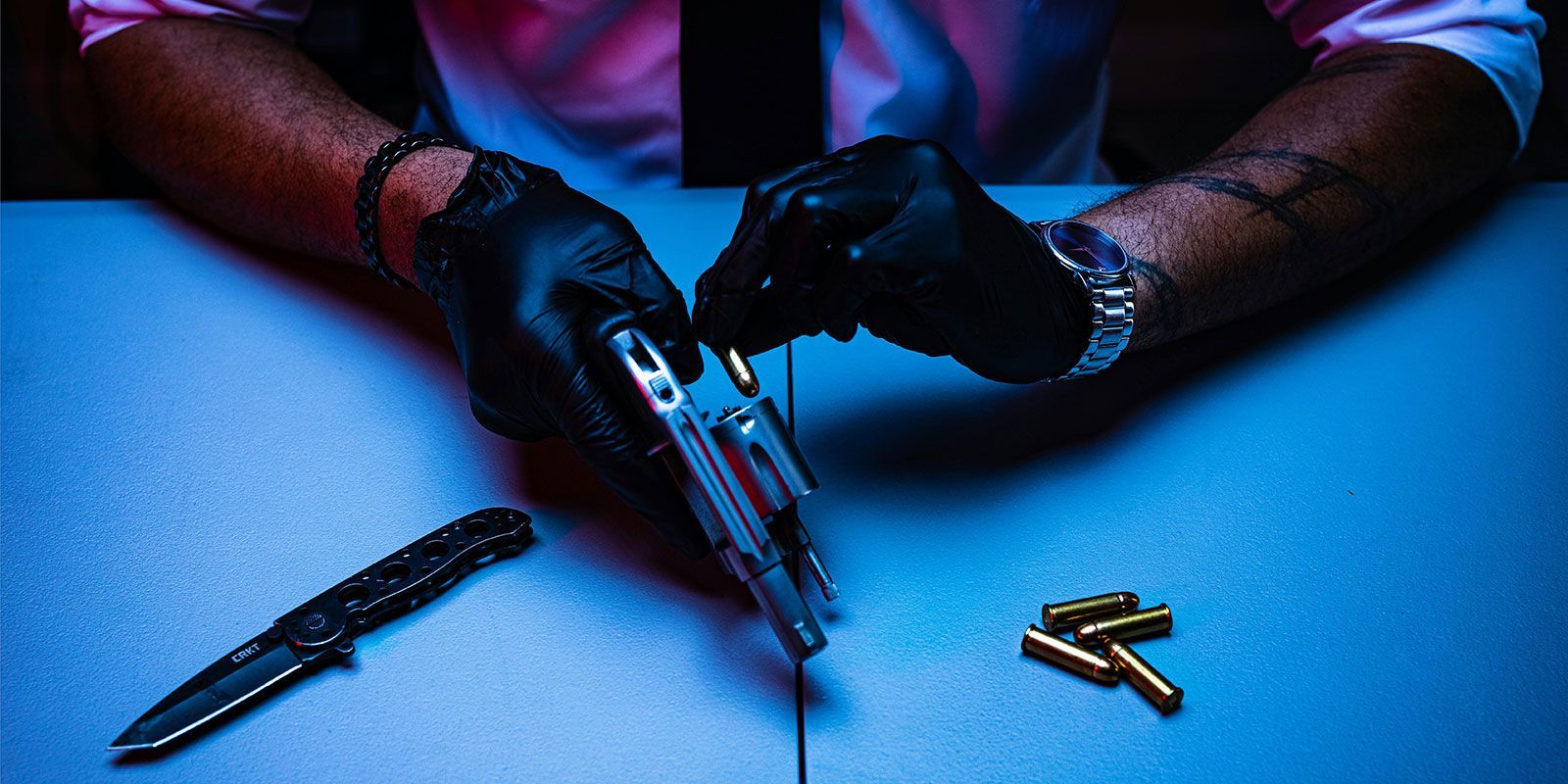 Close-up image of a man's arms and hands, he is loading a gun