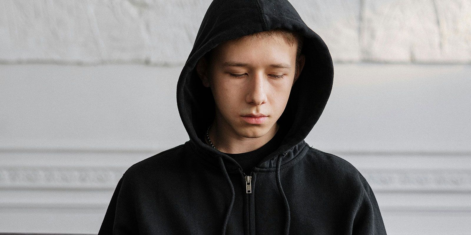 Head and shoulders of a boy wearing a hoodie, he's avoiding looking at the camera.