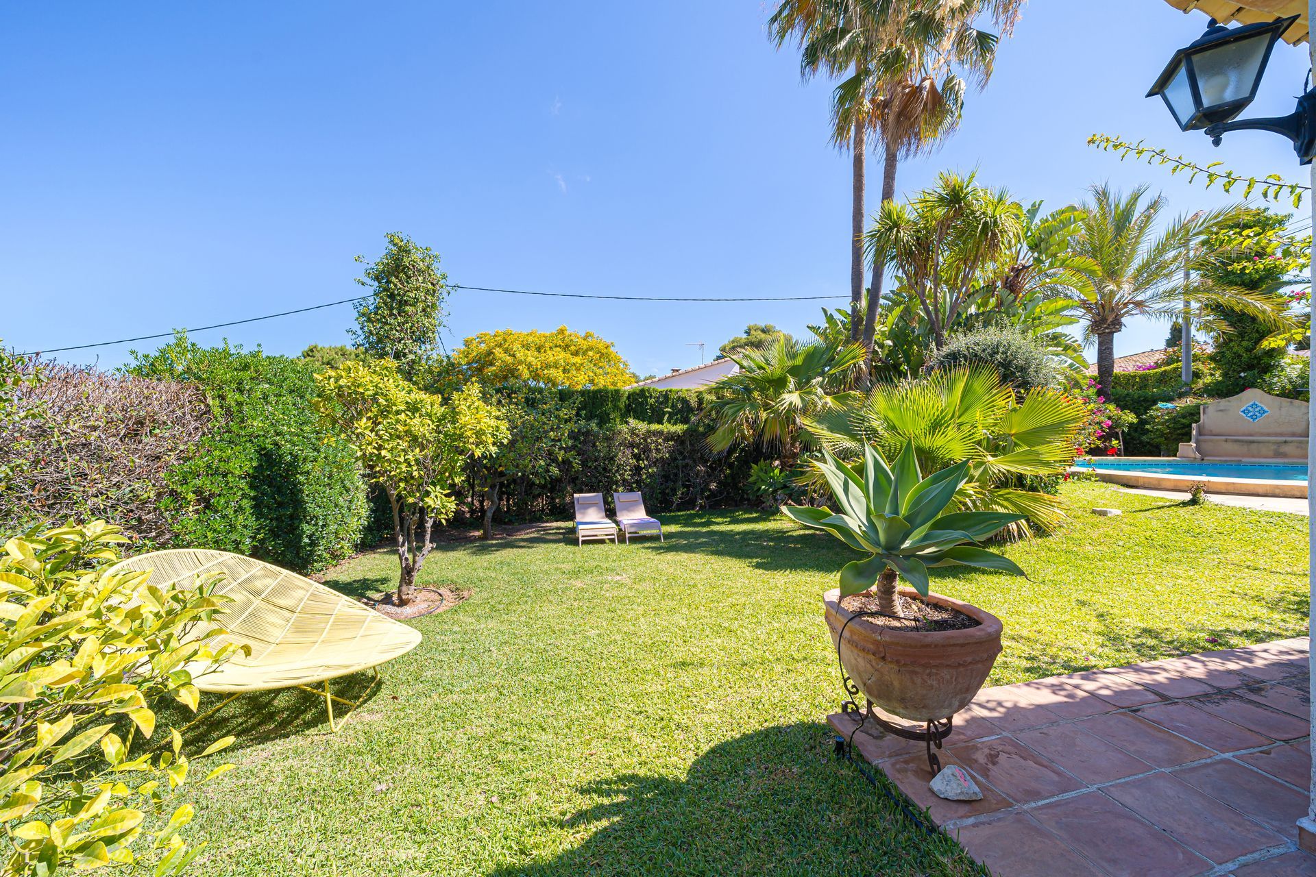 De weelderige groene tuin van Villa Fave Javea met een gele stoel op de achtergrond