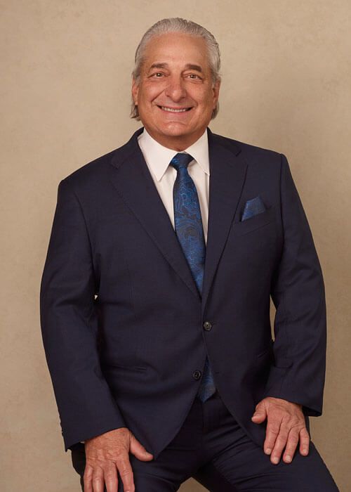Smiling person in a navy suit posing against a beige studio backdrop.
