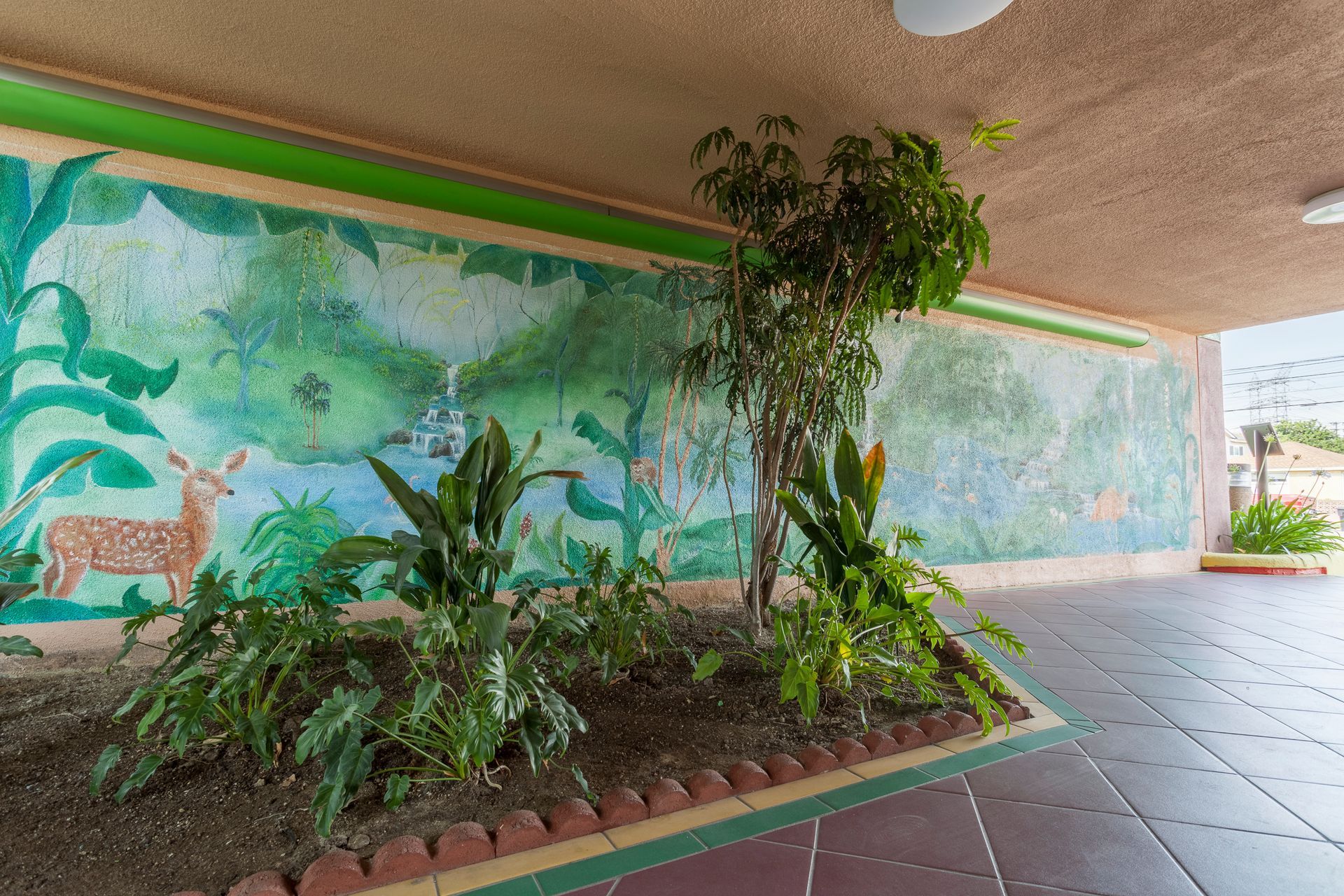 A mural on the wall of a building with plants in front of it.