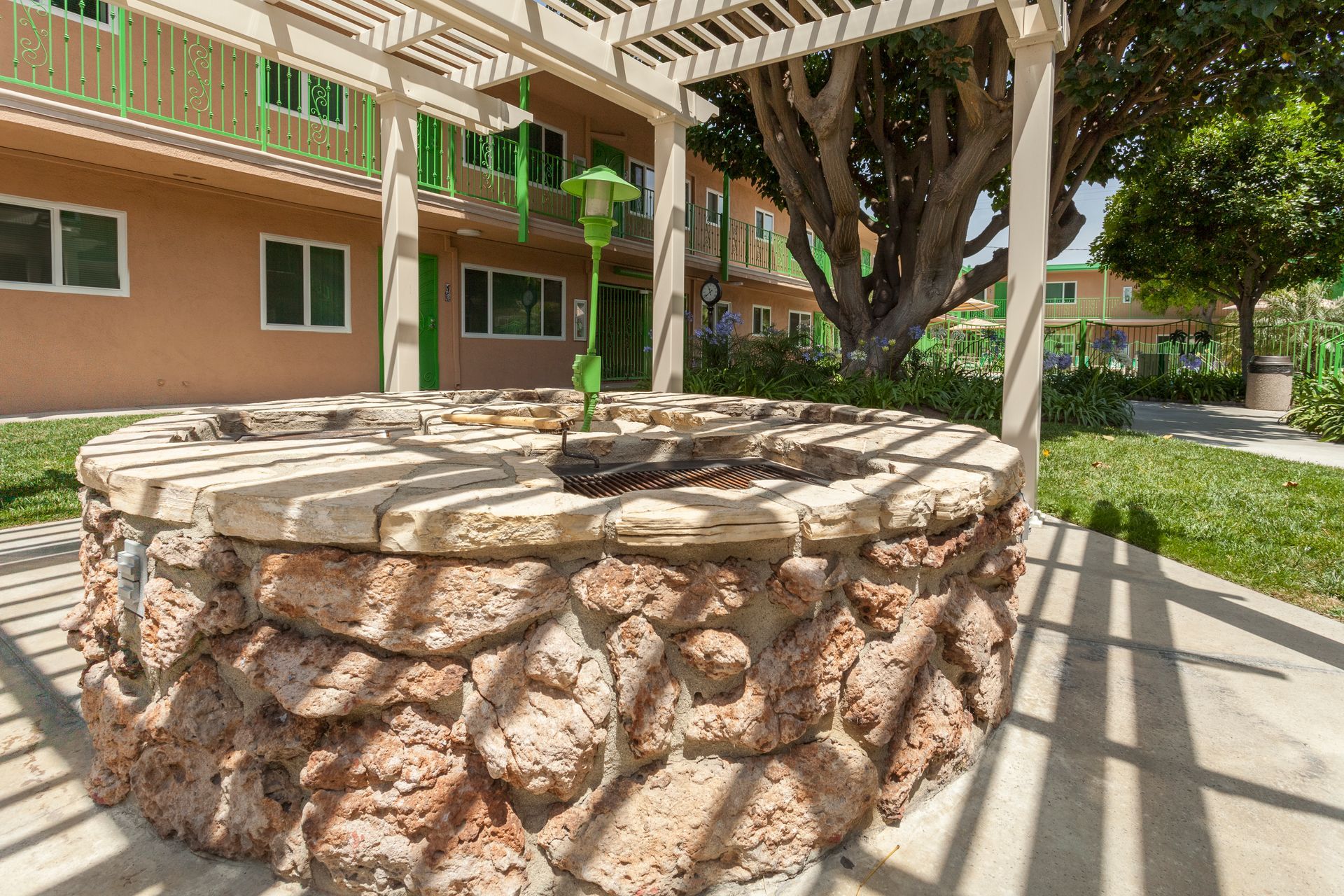 A stone fire pit is sitting under a pergola in front of a building.