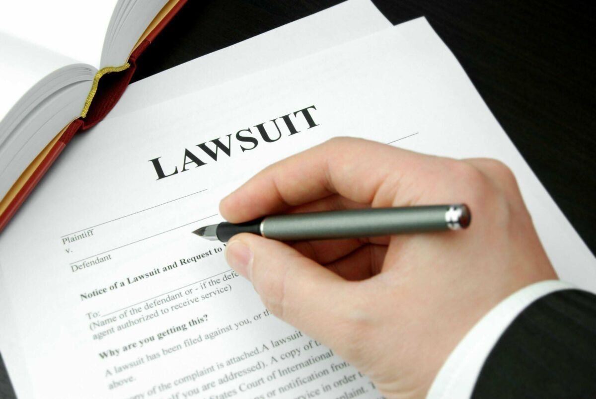 Hand writing on a lawsuit form with a pen, next to a legal folder