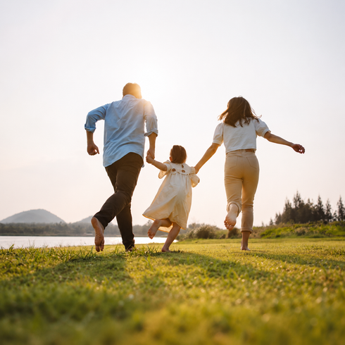 Family standing in a sunny field, parents holding a baby and smiling at each other