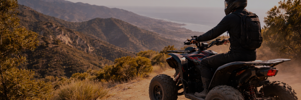 Quad rider overlooking a mountain valley at sunset, with golden hills and a distant lake