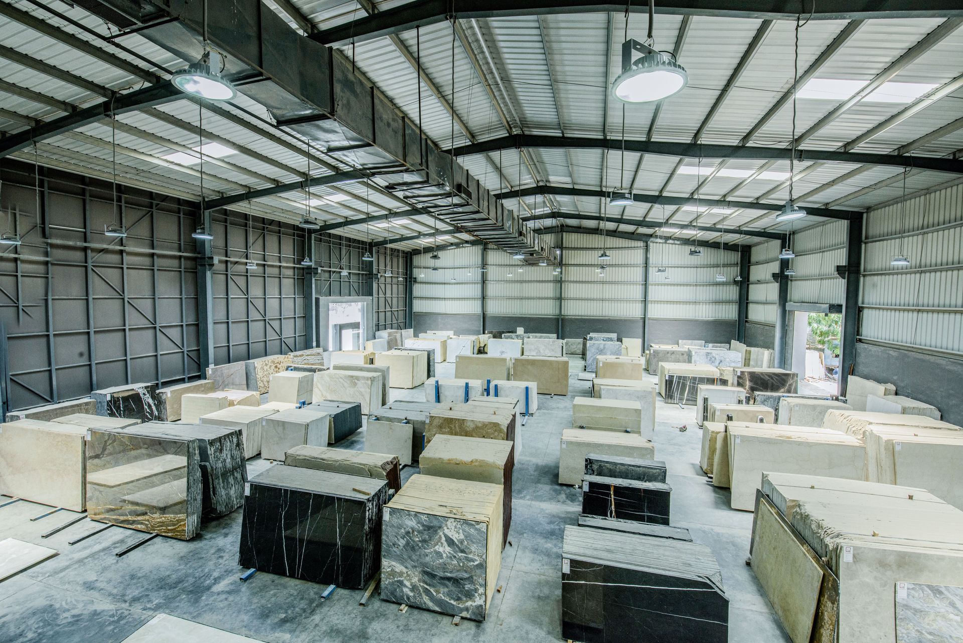 Warehouse interior with rows of wrapped pallets and stacked crates under metal beams and skylights