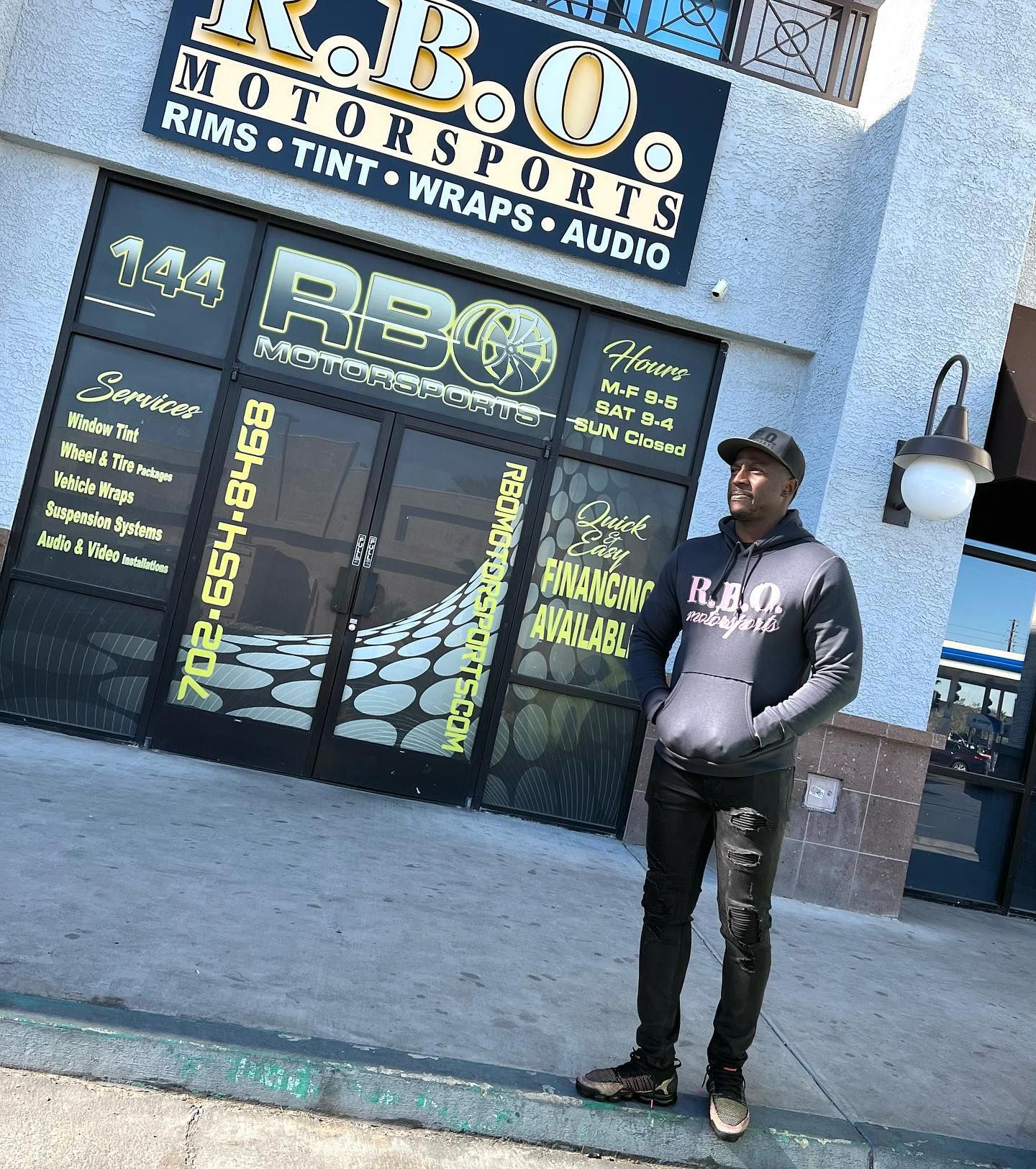 Man standing outside an R.B.O Motorsports storefront with black and yellow signage.