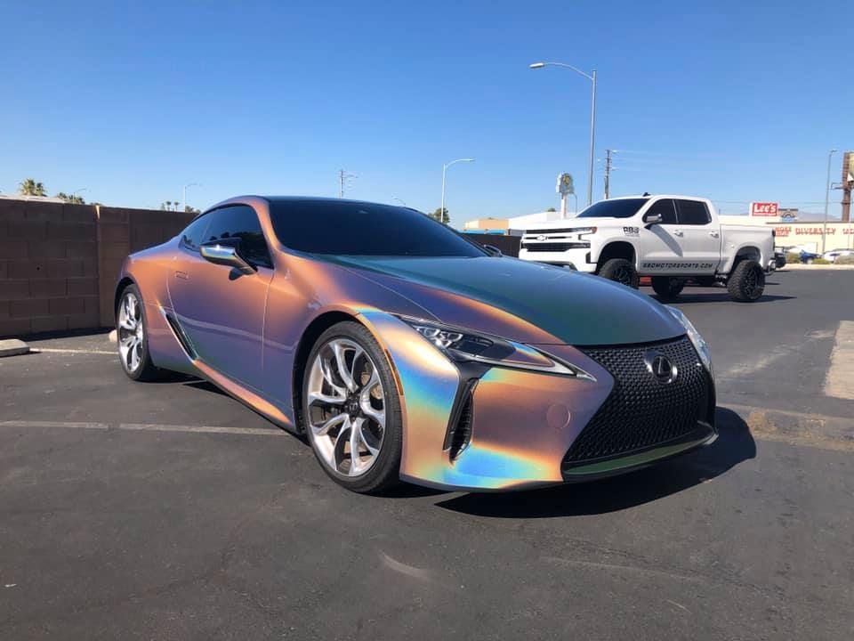 Shiny iridescent sports coupe parked in a lot under a clear blue sky