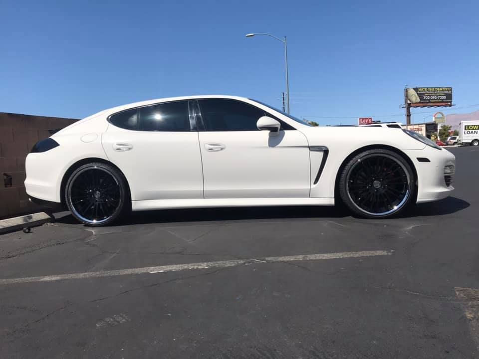 White lowered sports sedan parked in a lot under a clear blue sky.