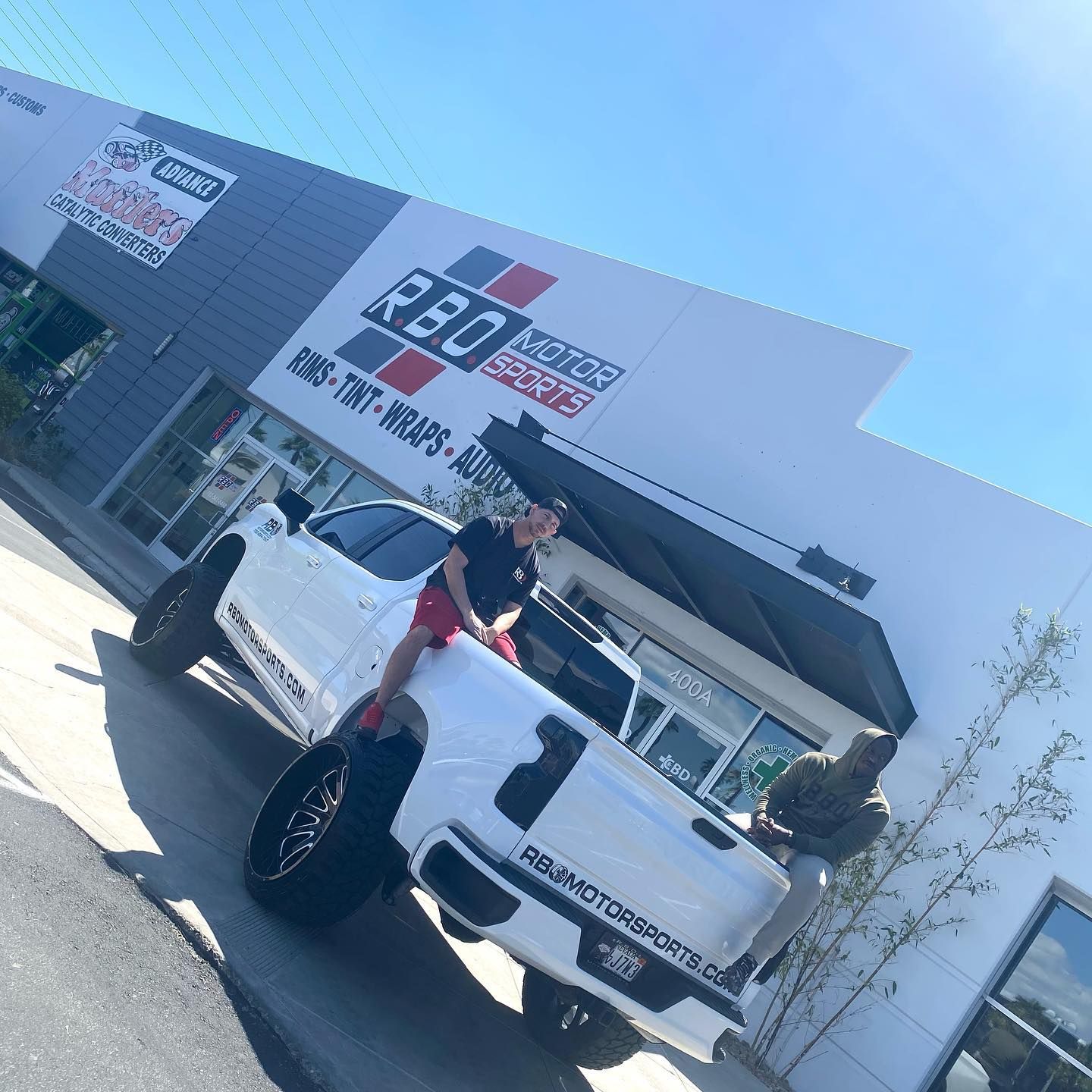 White lifted pickup truck parked outside a building with a large red-and-black sign