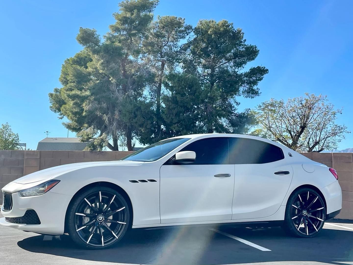 White sedan parked in a lot under a blue sky with trees in the background