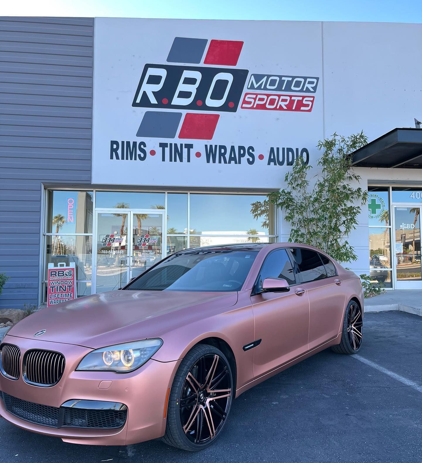 Pink BMW sedan parked outside RBO Motorsports storefront with rims, tint, wraps, and audio signage