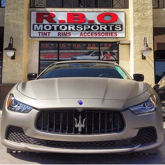 Silver Maserati parked in front of R.B. Motorsports shop sign