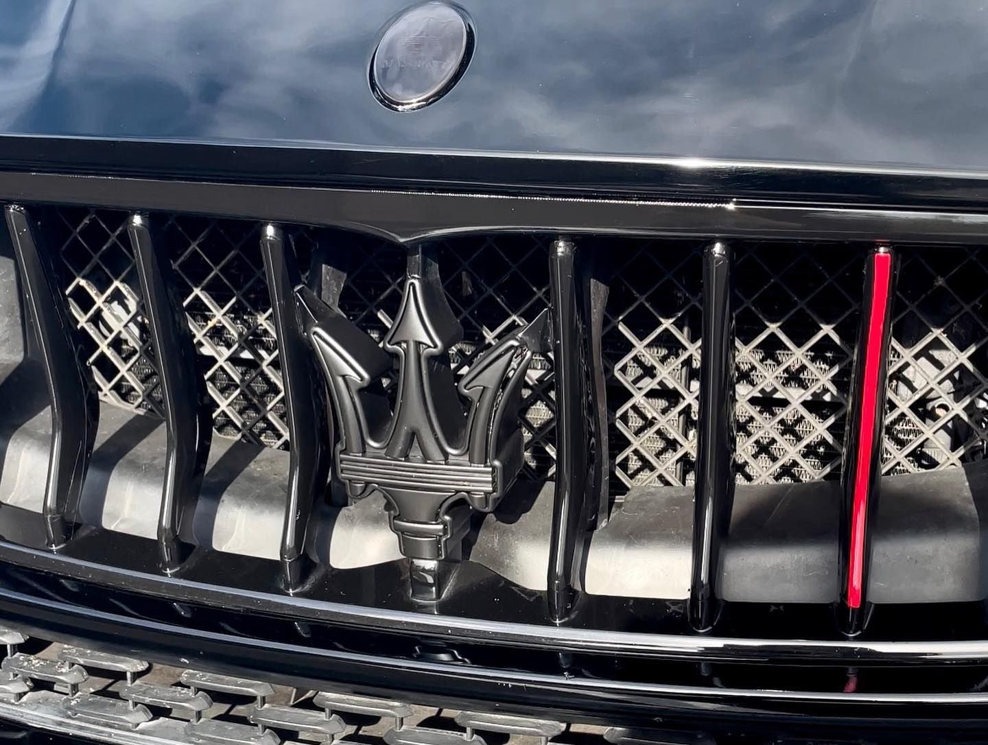 Close-up of a black car grille with a silver emblem and red accent stripe