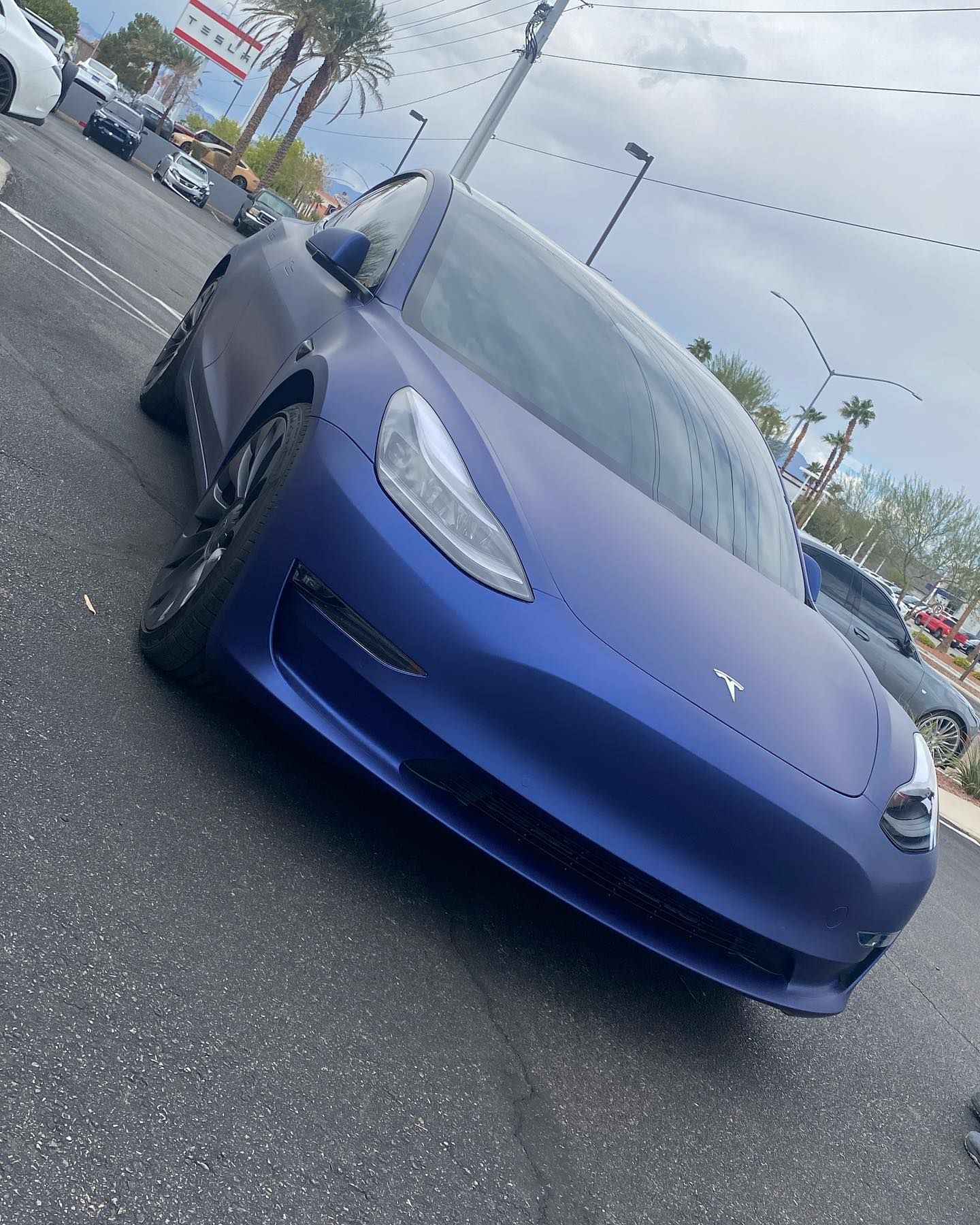 Blue Tesla parked in a lot, front angled view on a cloudy day.