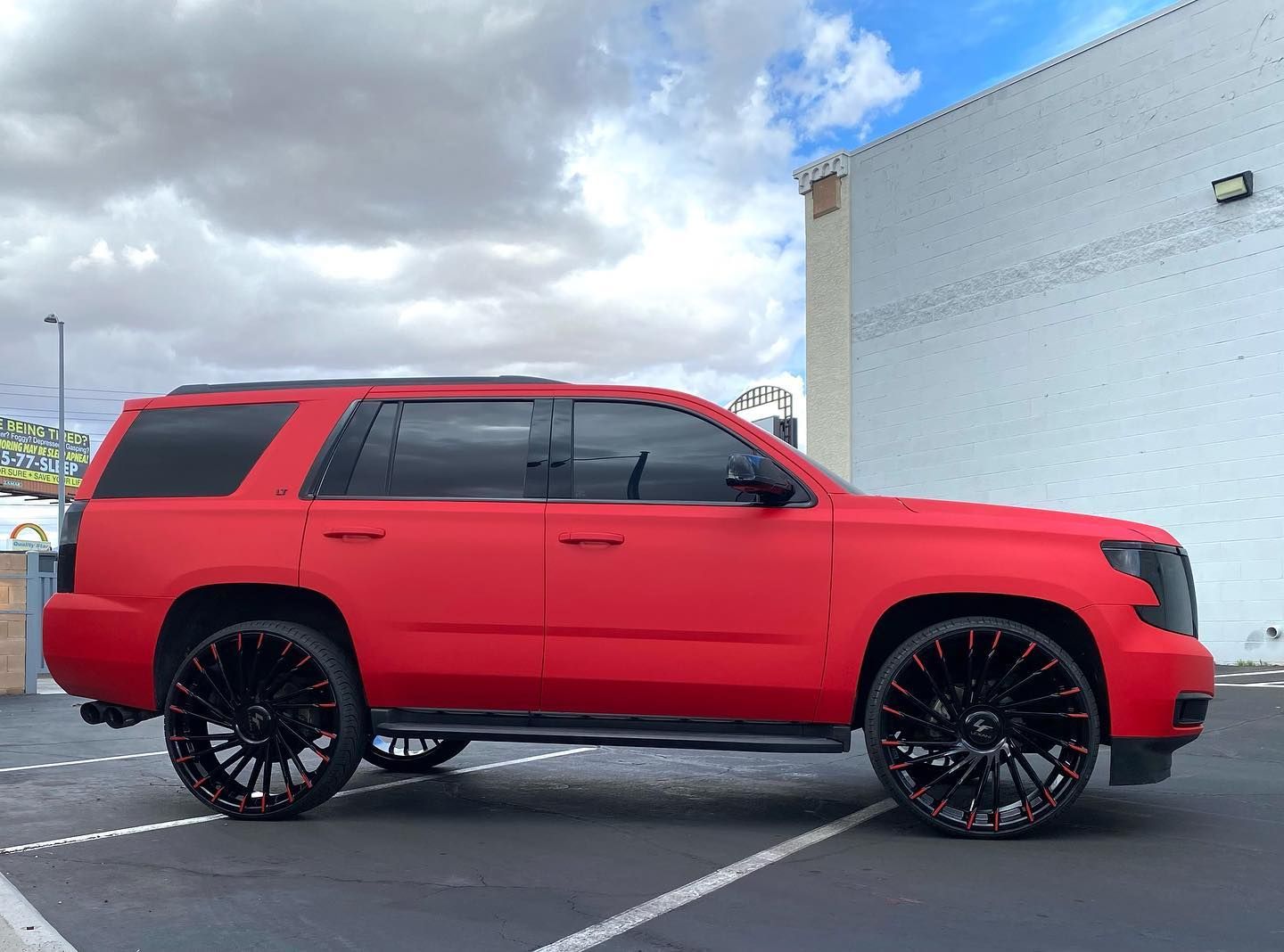 Red SUV with black rims parked beside a white building under a cloudy sky