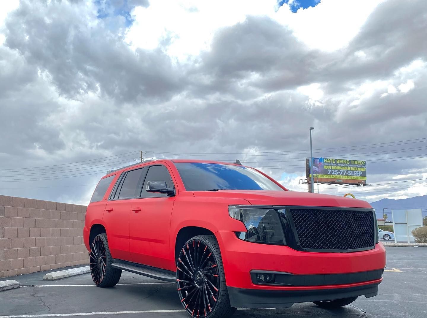 Red SUV with black wheels parked on a road under a cloudy sky.