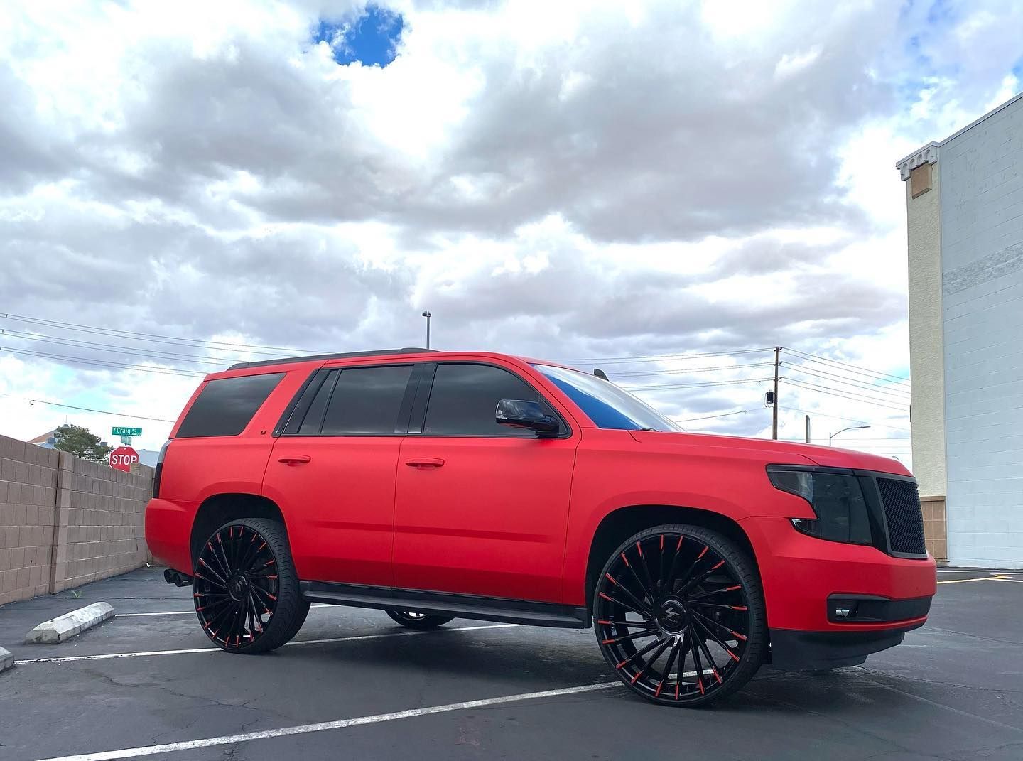Red SUV parked in a lot under a cloudy sky, with black rims and tinted windows.