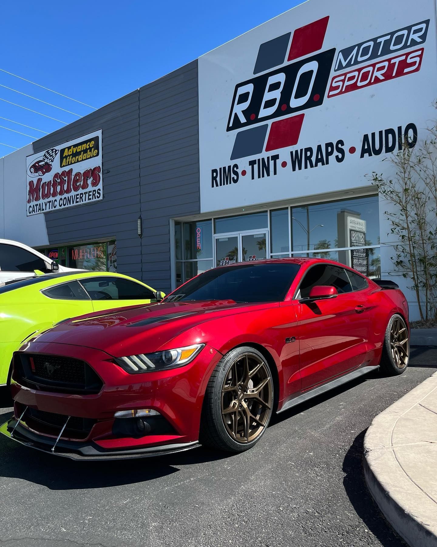 Red sports car parked outside RED Motor Sports shop with signage for rims, tint, wraps, and audio