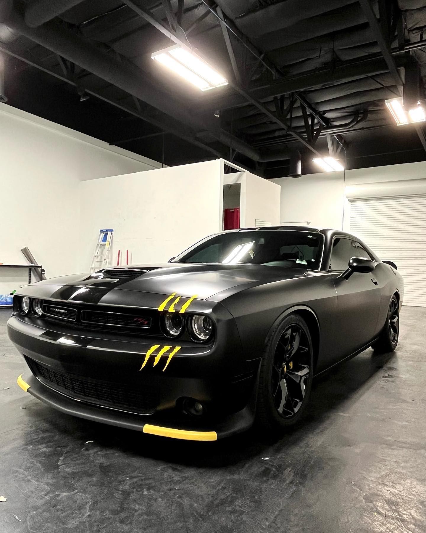 Black Dodge Challenger with yellow racing stripes parked indoors under bright lights