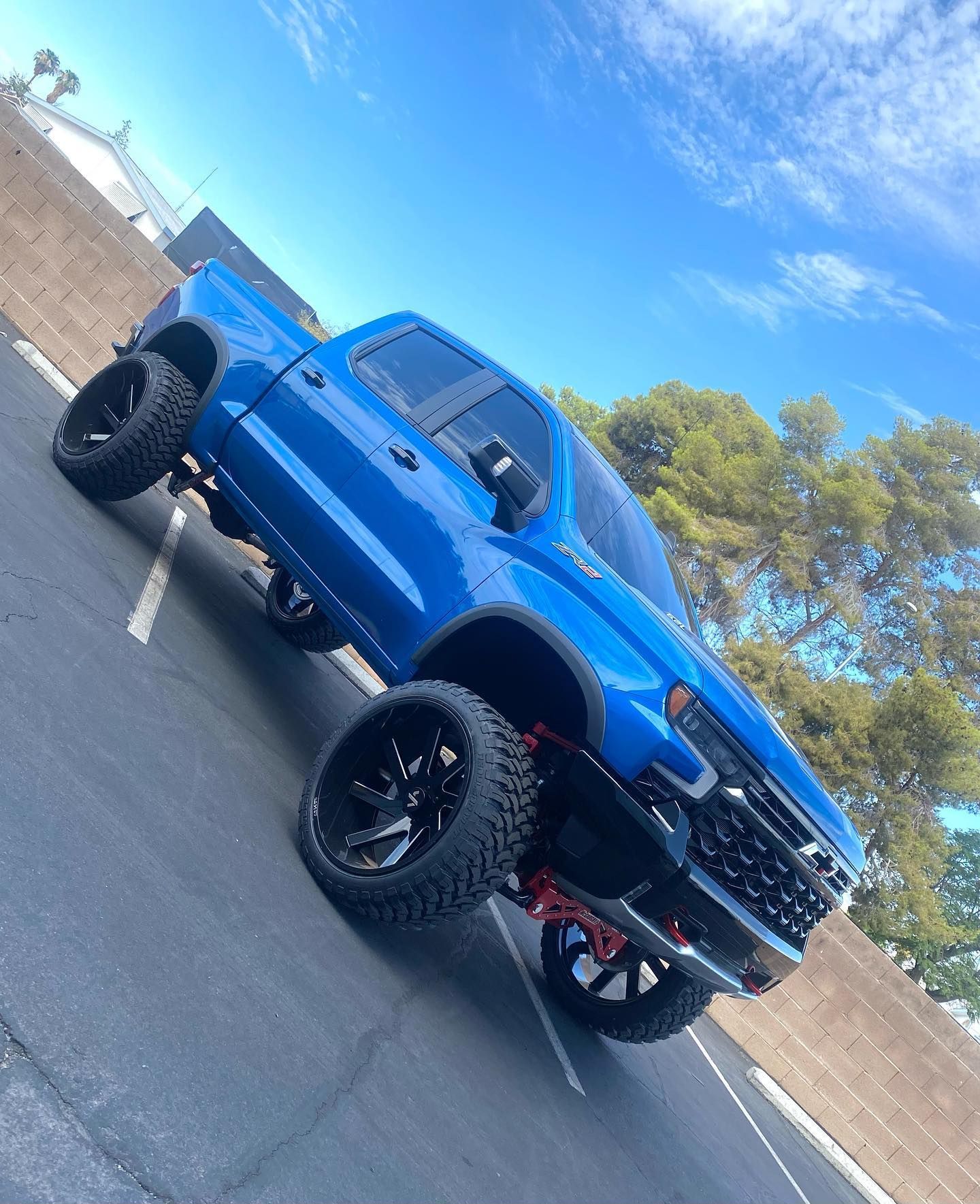 Blue lifted pickup truck parked in a lot under a bright blue sky