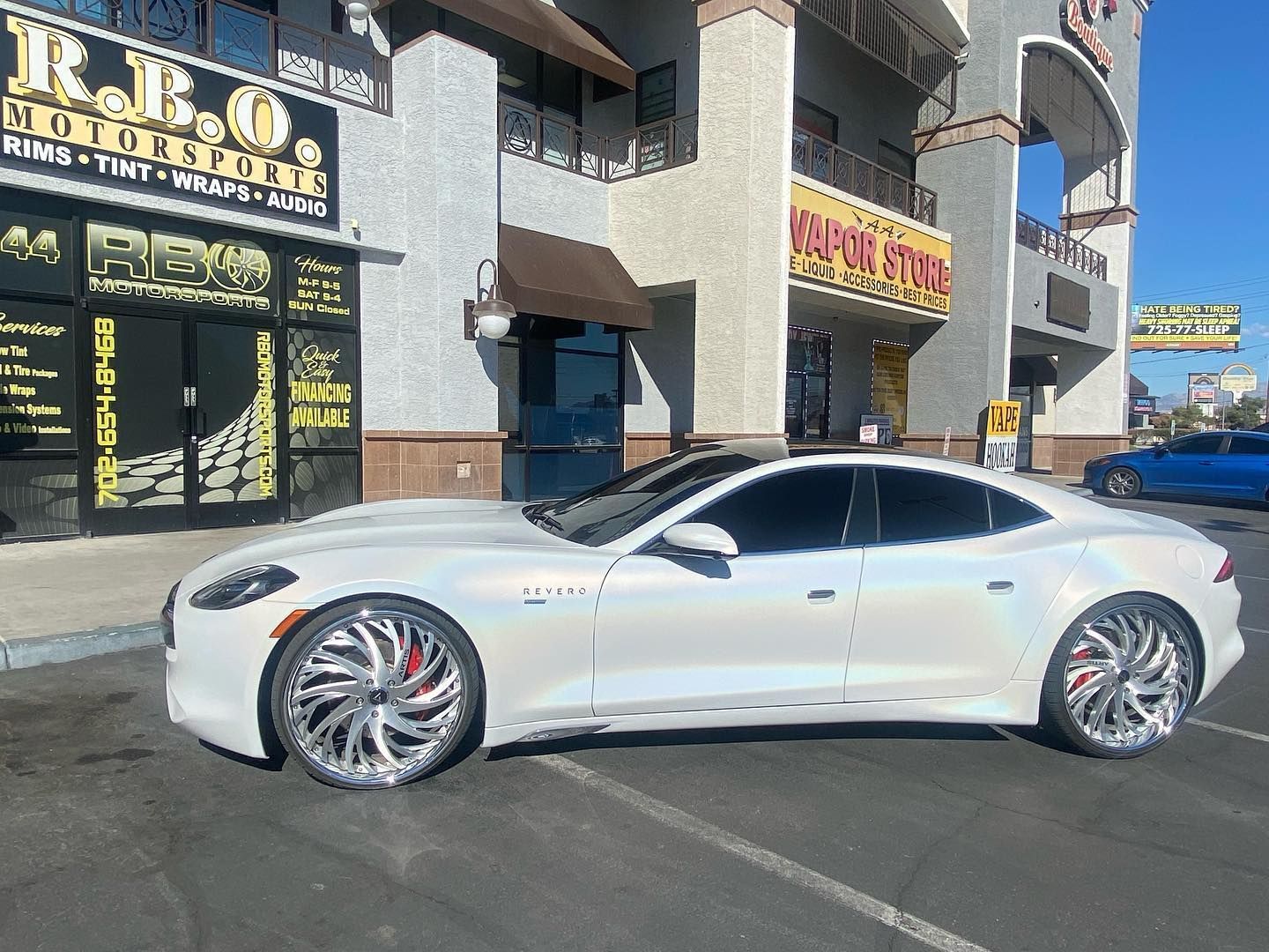 White sedan parked on a sunny street in front of storefronts and apartment buildings