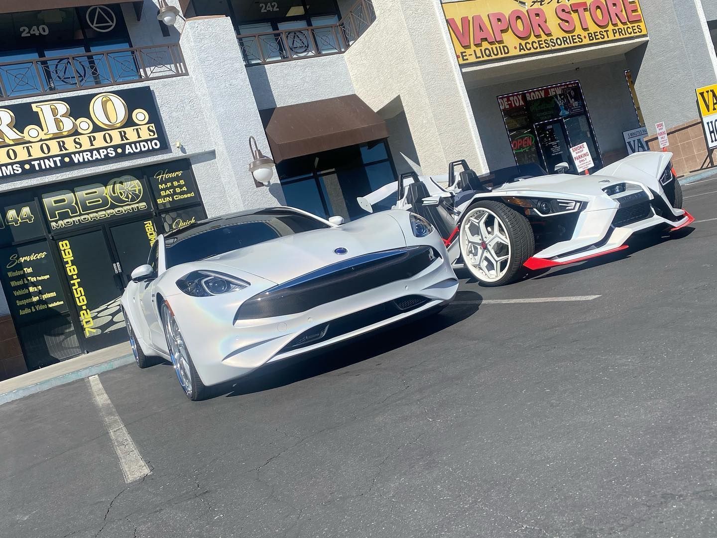 Two white sports cars parked outside a storefront on a sunny street