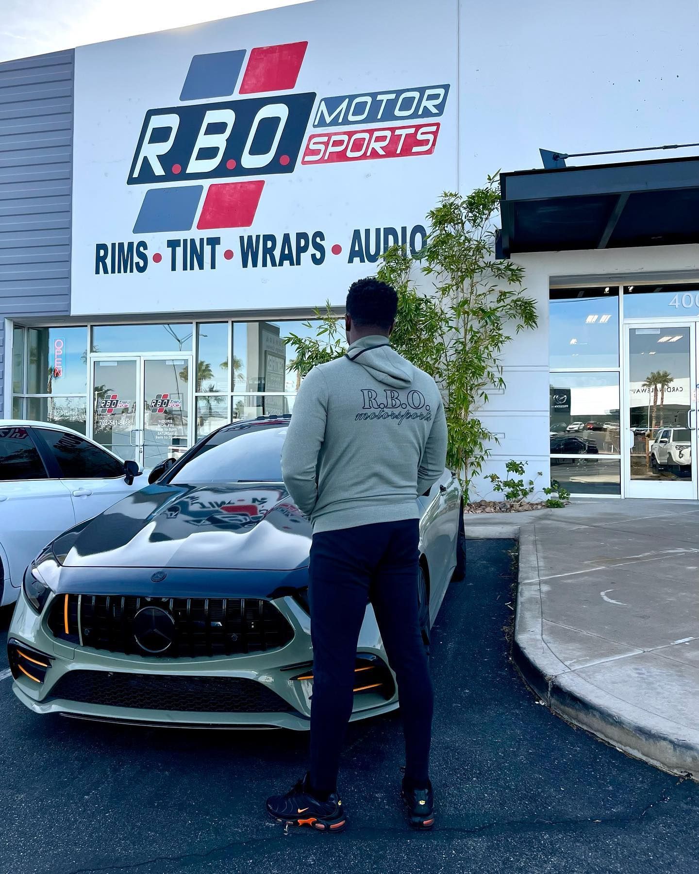 Person standing in front of a black sports car outside R&D Motors shop