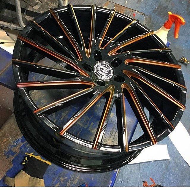 Black multi-spoke alloy wheel rim with copper accents on a blue floor
