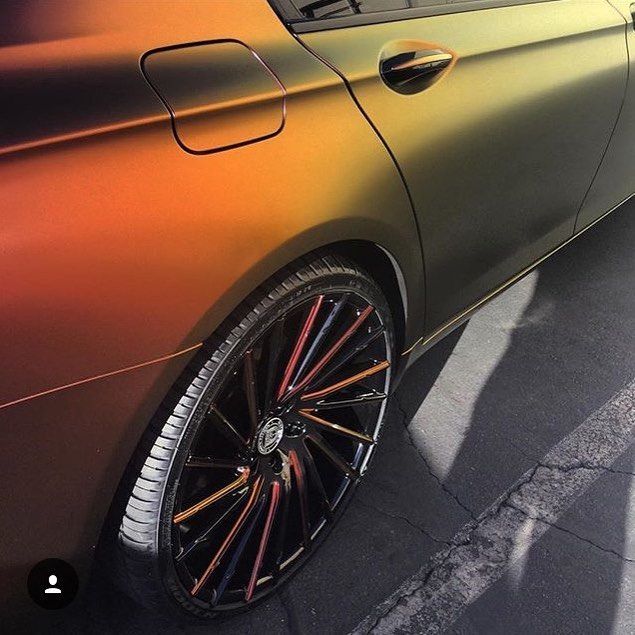 Close-up of a matte bronze sports car side panel and rear wheel with black and red rims.